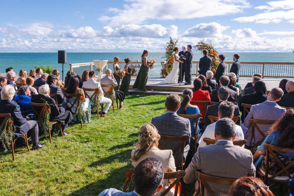Outdoor wedding ceremony on a grassy cliff overlooking the ocean, with guests seated in rows facing the altar.