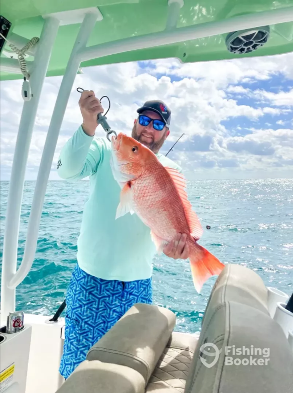 Angler holds up a red snapper fish on a center console boat in turquoise offshore waters.