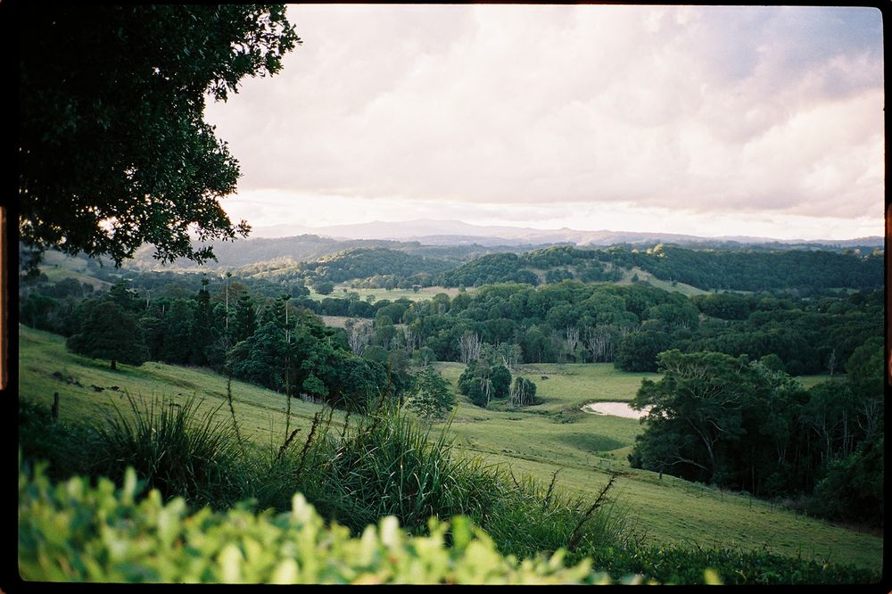 Lush green rolling hills and valleys stretch beneath a cloudy sky in a scenic countryside landscape.
