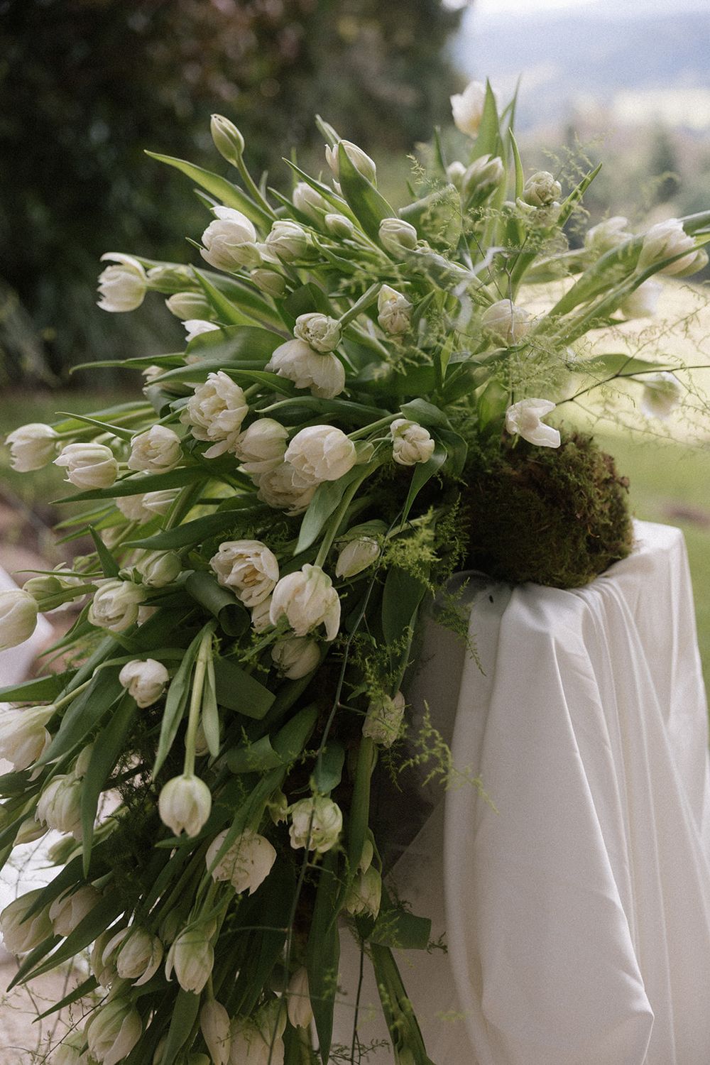 Elegant white tulip floral arrangement cascading over a white draped table at an outdoor wedding ceremony.