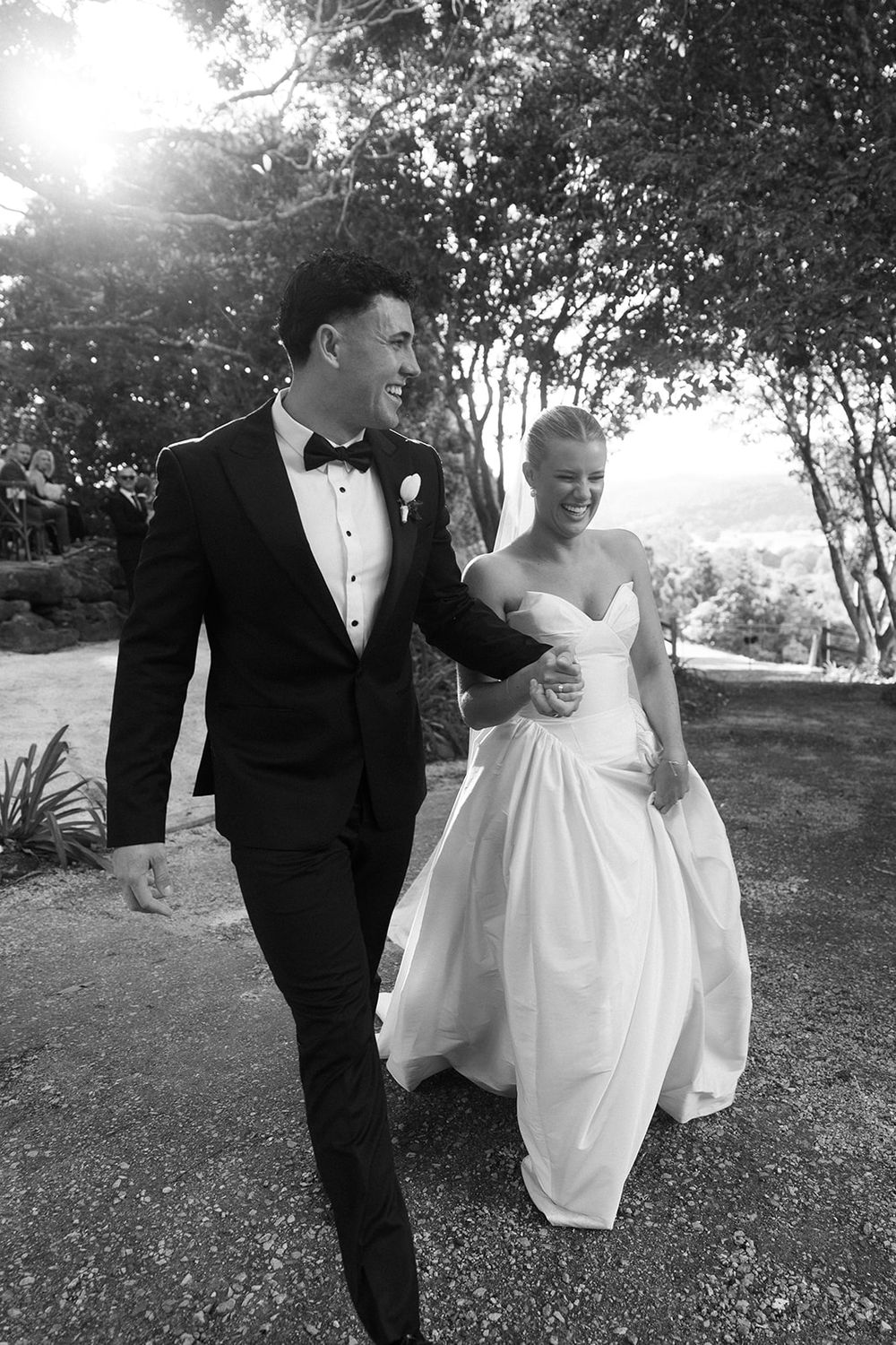 Black and white photo of a smiling bride and groom walking together outdoors on their wedding day.