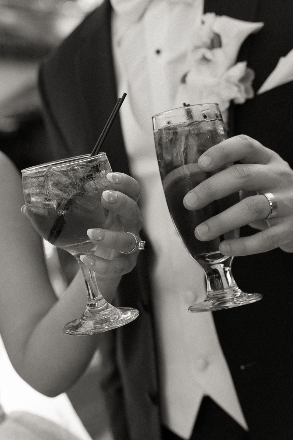 Black and white photo of bride and groom holding cocktail glasses at wedding reception.