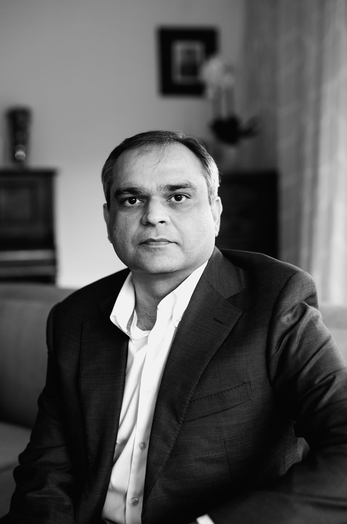 Black and white portrait of a professional man in a blazer and dress shirt seated indoors.