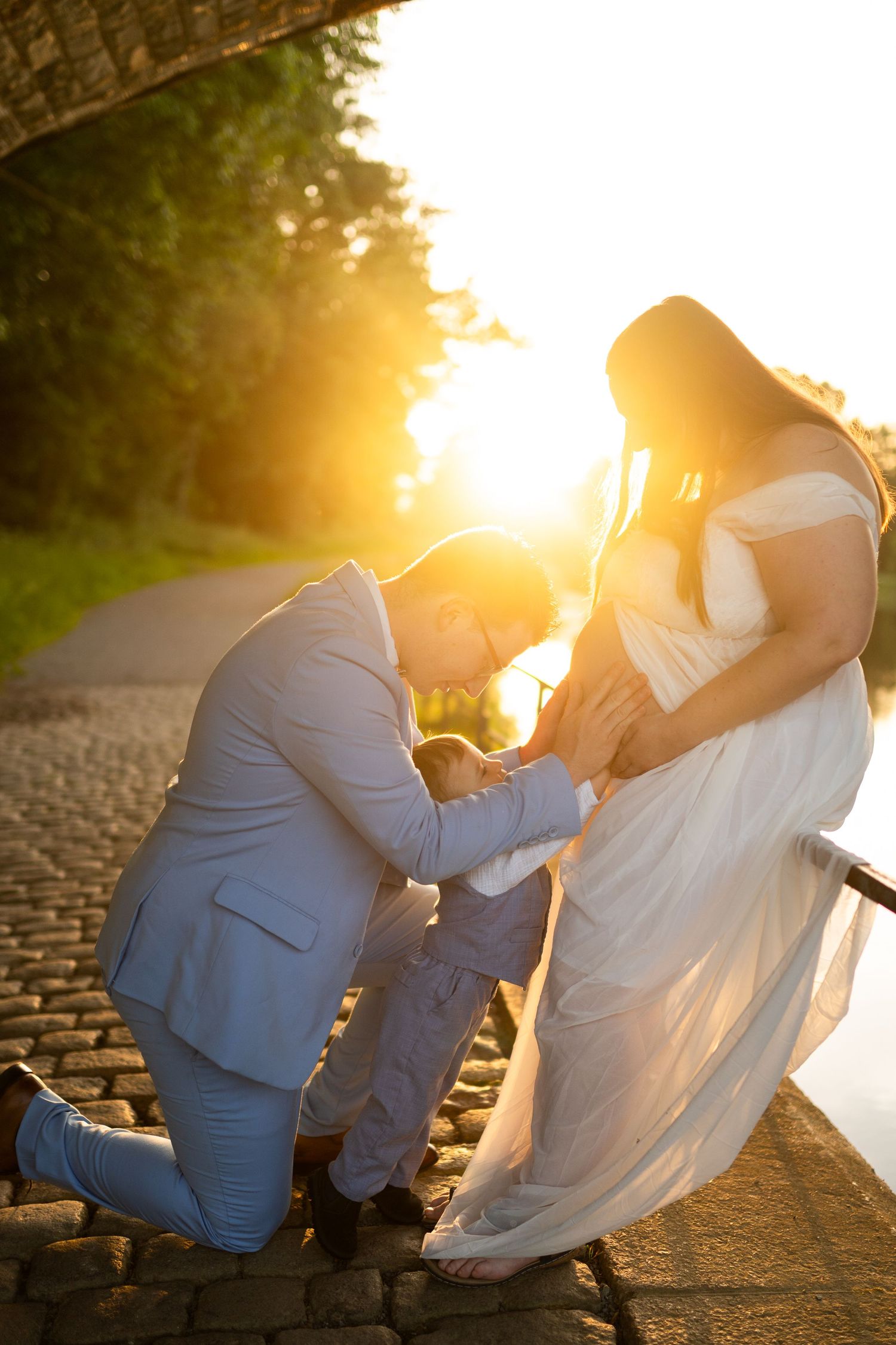 Le marié s'agenouille devant la mariée en robe blanche pendant le coucher de soleil doré sur un chemin pavé, photo de mariage à Rennes.