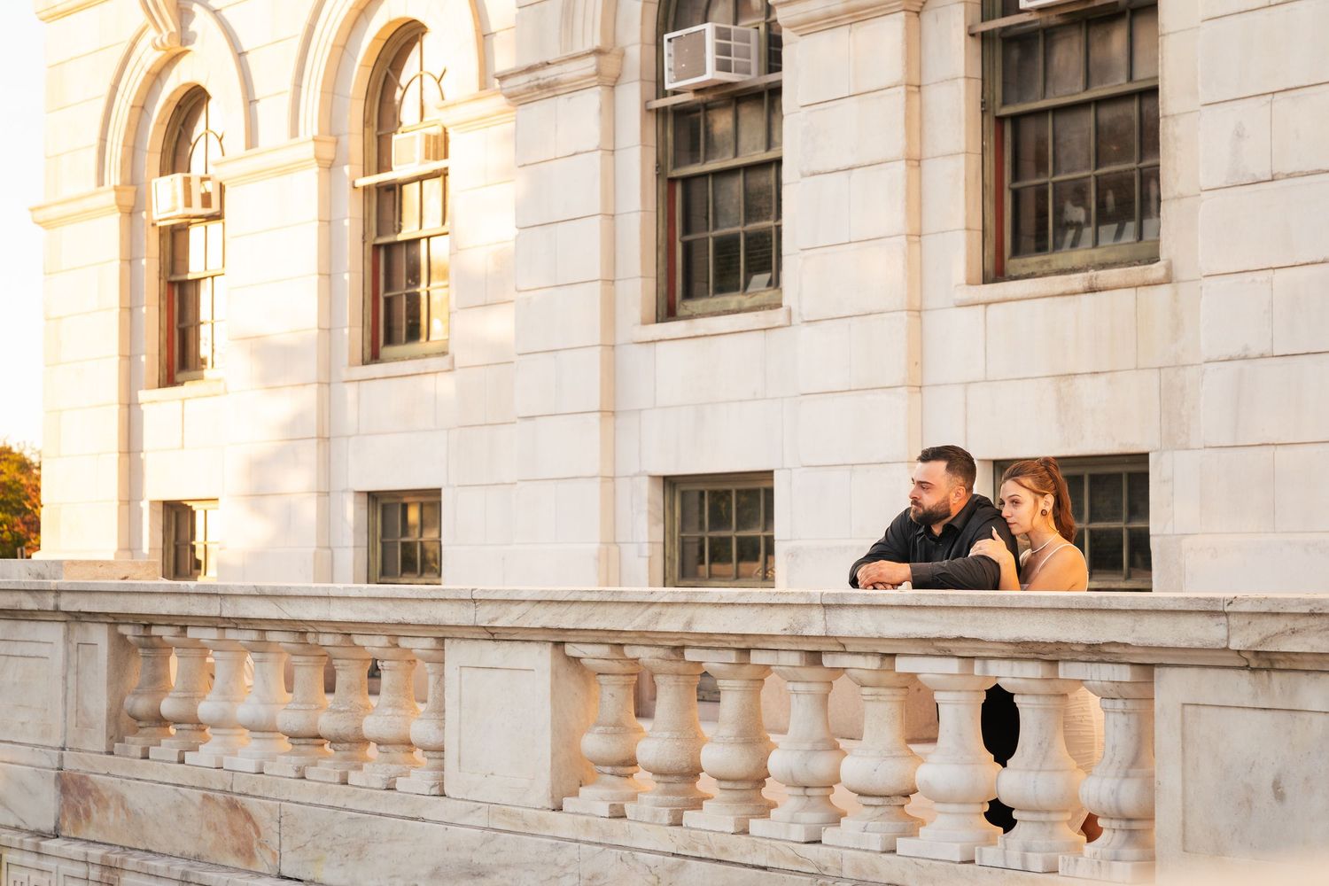 Couple leaning on ornate marble balustrade of a grand historic building during golden hour engagement photo.