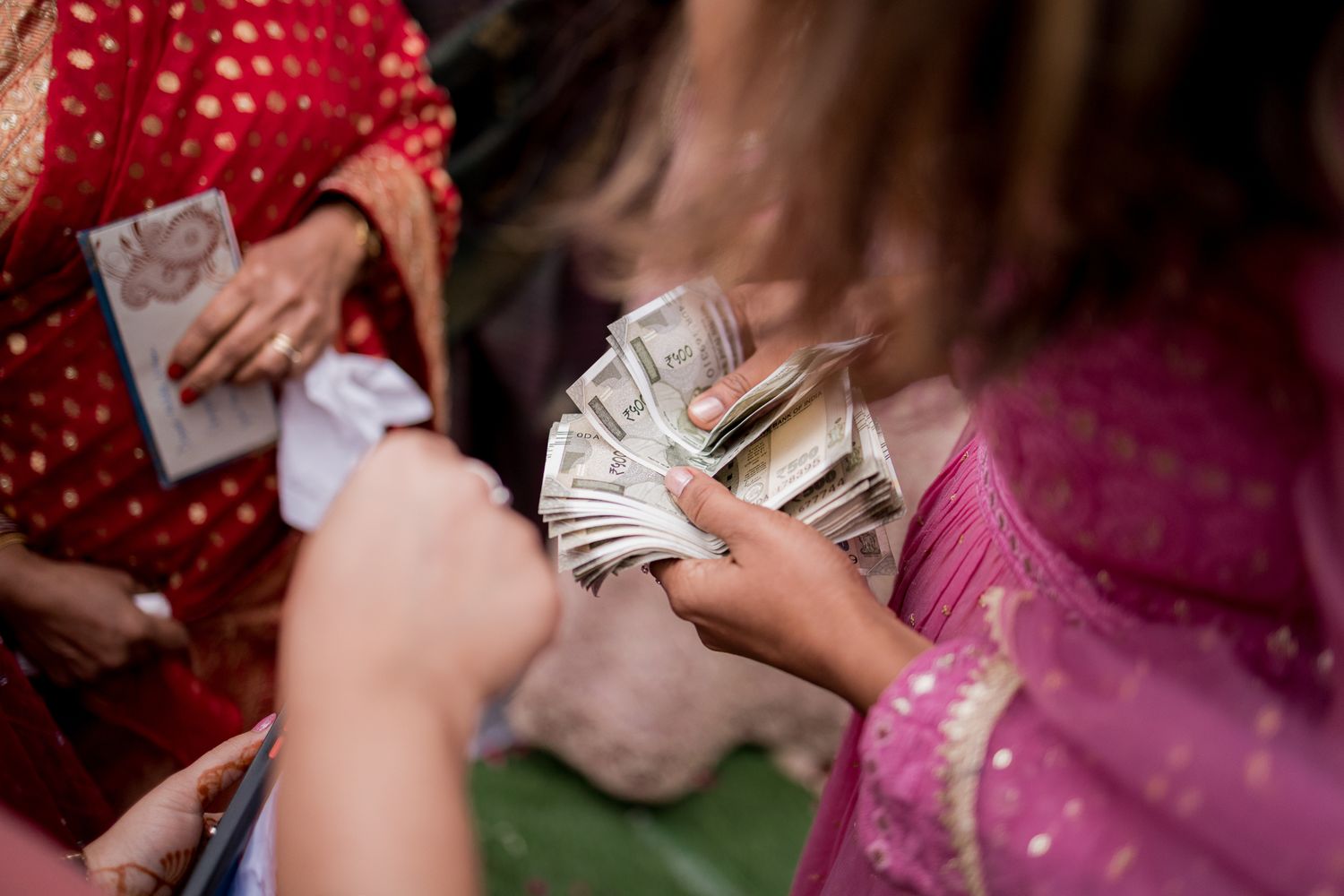 Women in traditional South Asian attire exchanging US dollar bills during a cultural celebration or wedding ceremony.