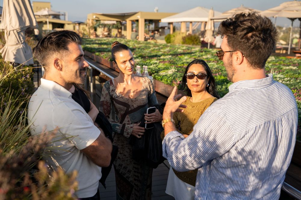Four friends socializing outdoors at a rooftop garden party on a sunny day.