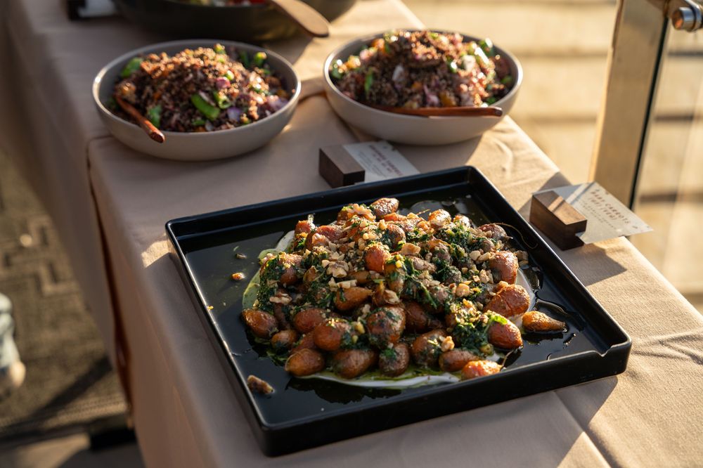 Catered buffet spread featuring roasted vegetable grain bowls with chickpeas and fresh herbs on an outdoor table.