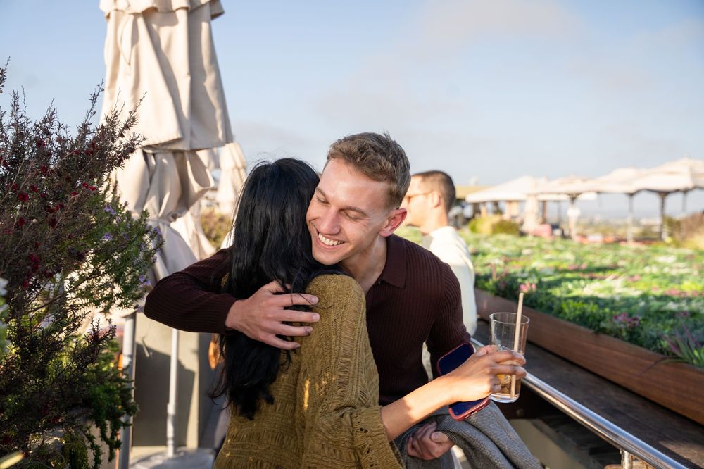 Two people sharing a warm hug at an outdoor rooftop event on a sunny day.