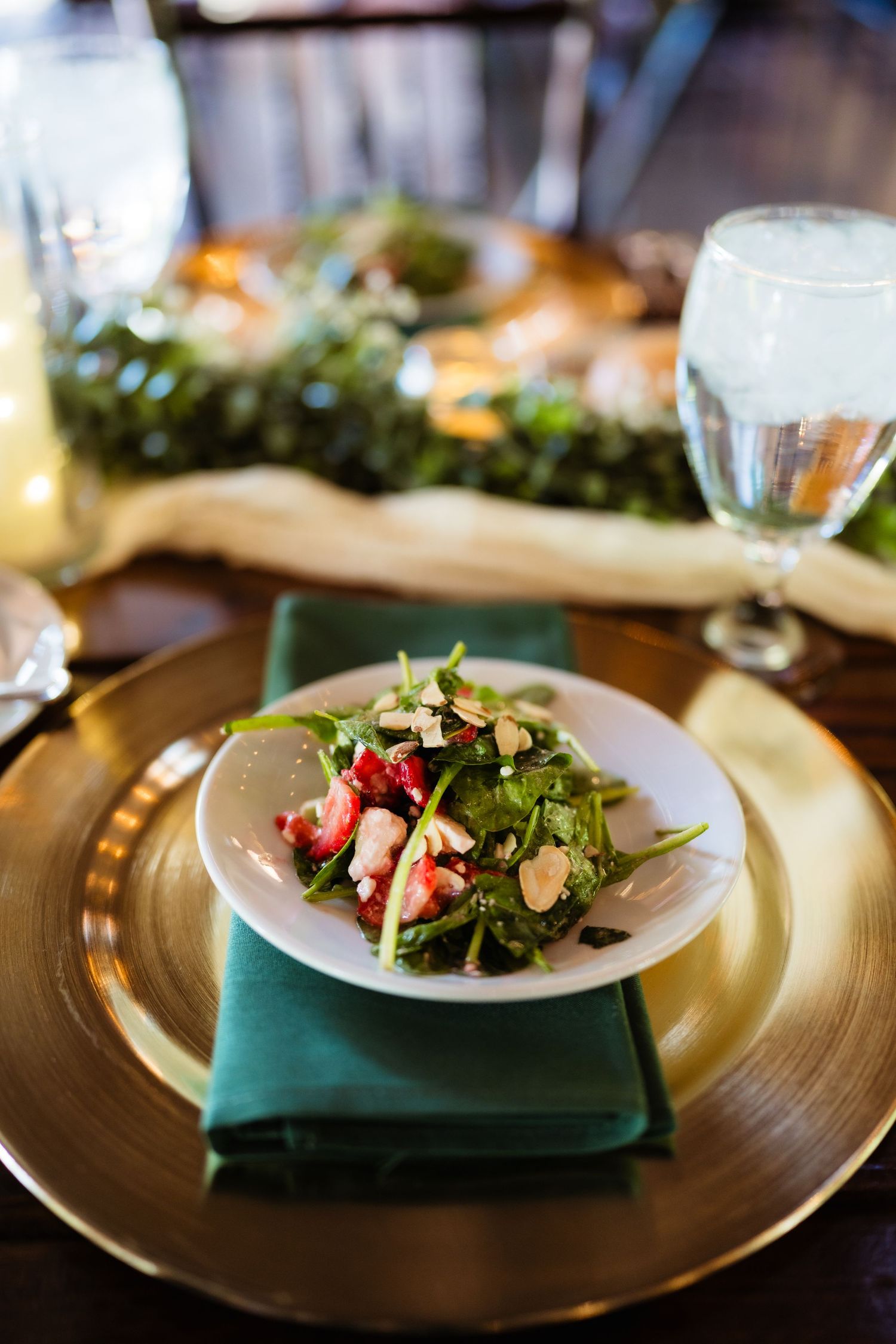 Elegant salad with greens, strawberries, and almonds on white plate, gold charger, green napkin, formal table setting.