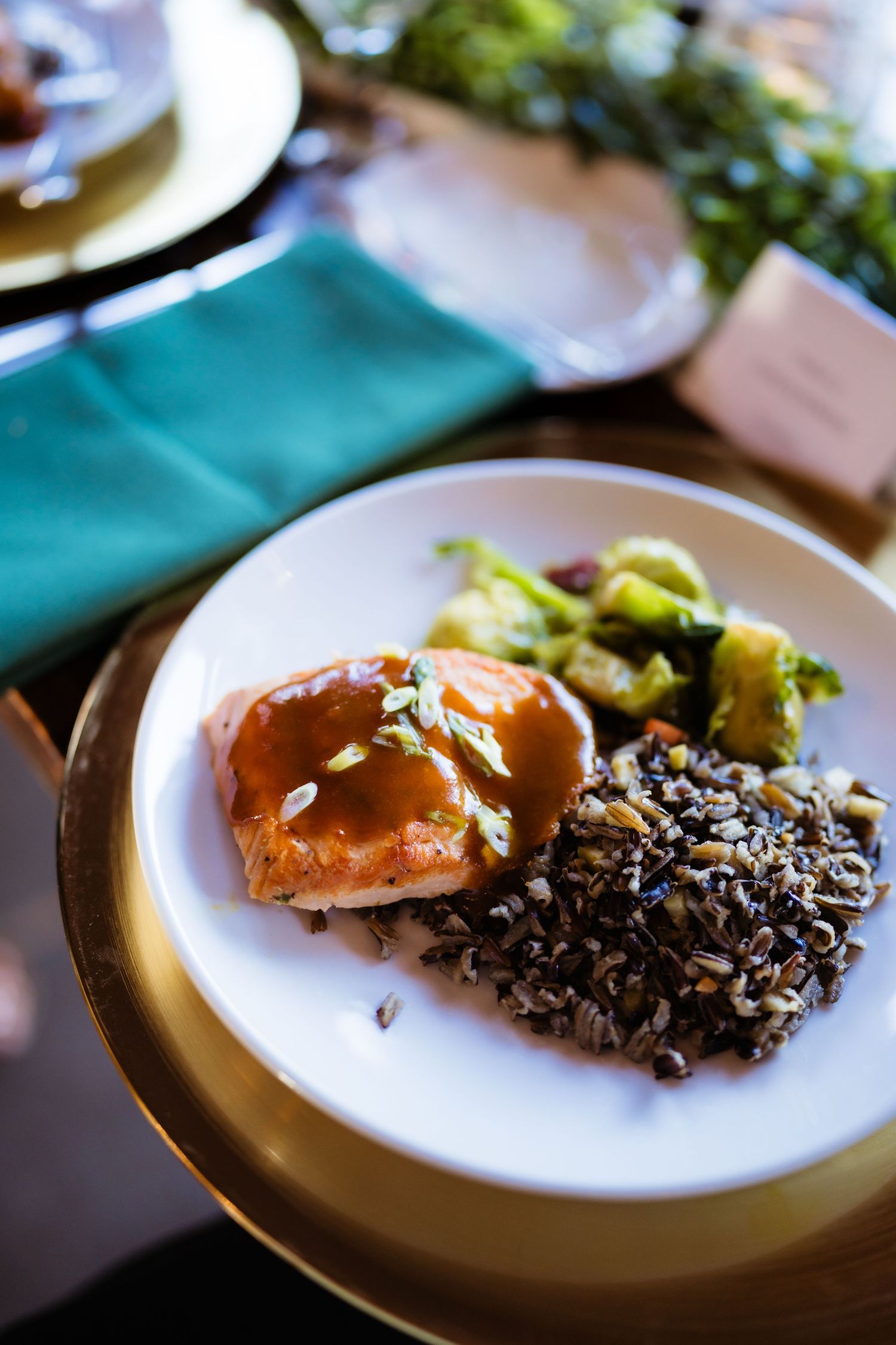 Elegant plated dinner with glazed salmon, wild rice, and roasted vegetables on a white and gold plate.