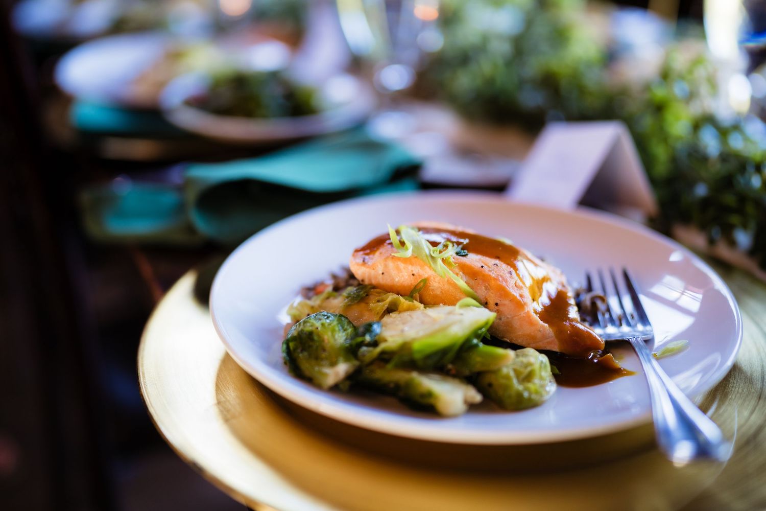A plated dish with salmon, roasted Brussels sprouts, and sauce served on a white plate at an elegant dinner table.