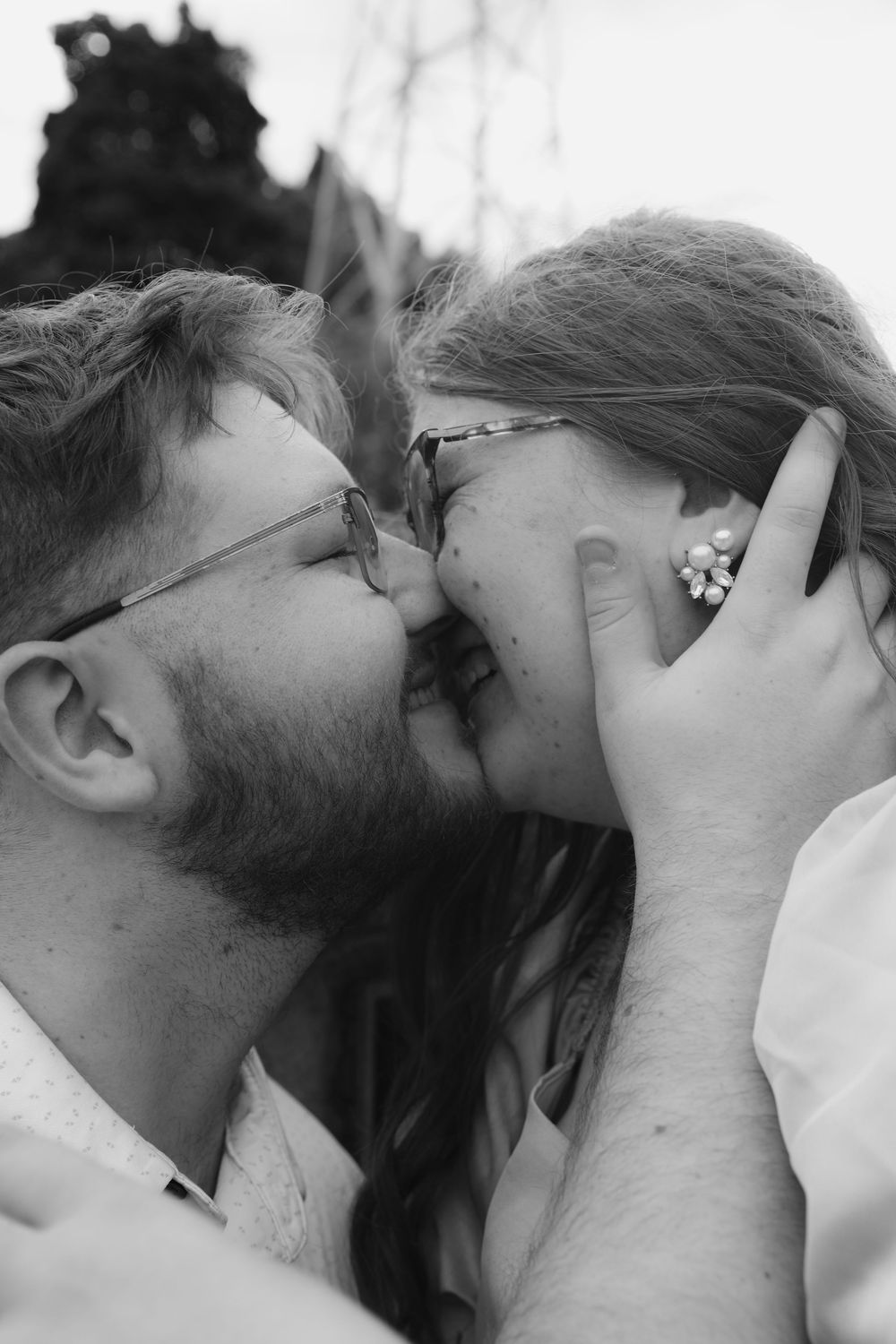 Black and white photo of couple sharing a tender kiss, man wearing glasses with beard.