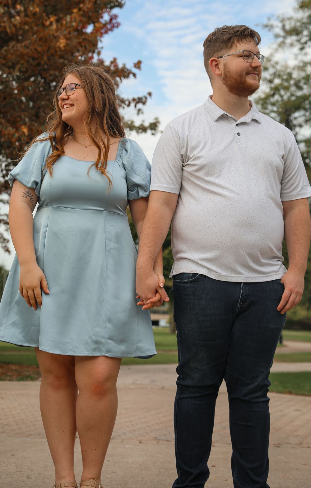 Happy couple holding hands in a park, woman in light blue dress, man in white polo.