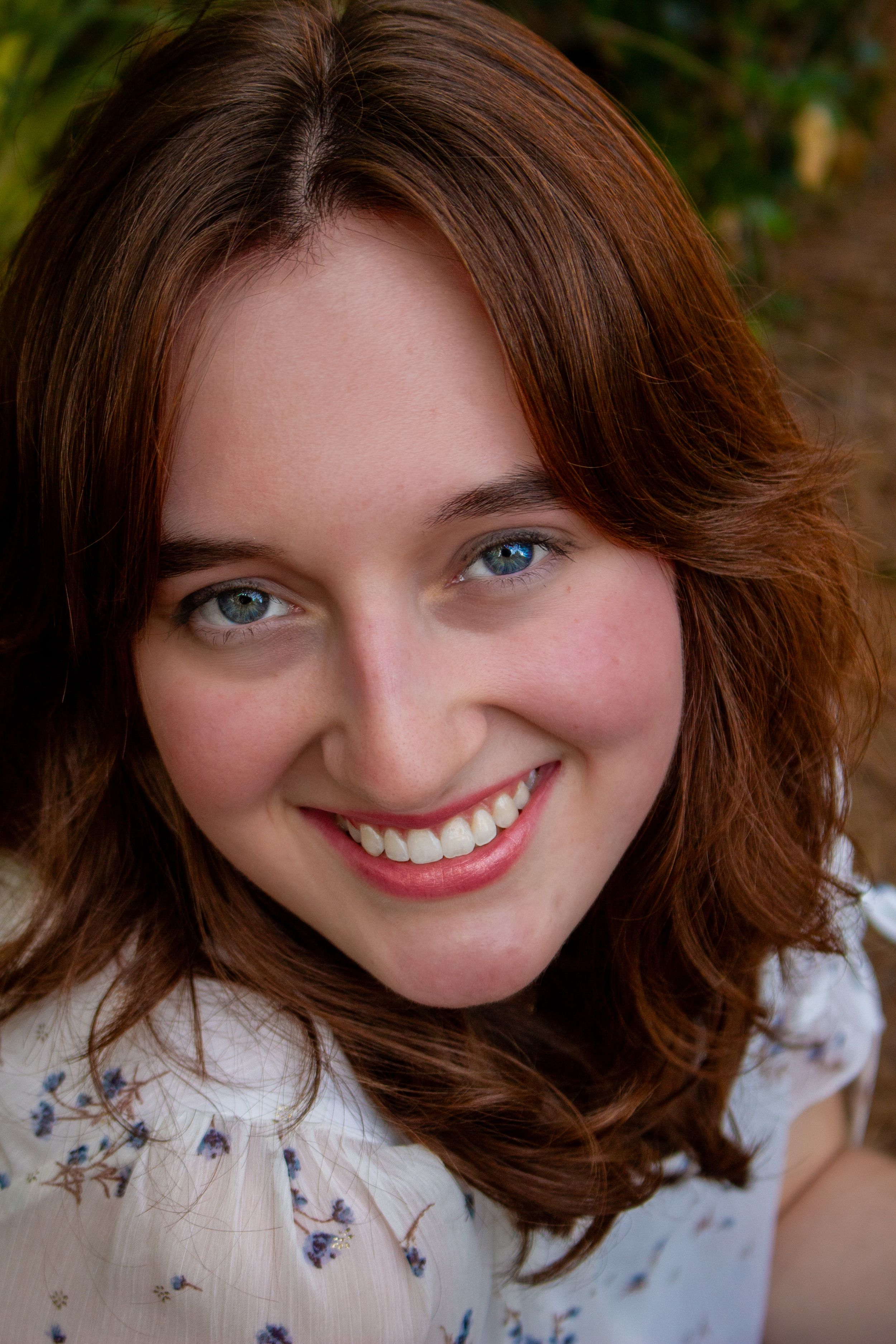 Close-up portrait of a smiling young woman with blue eyes and auburn hair wearing a floral top.