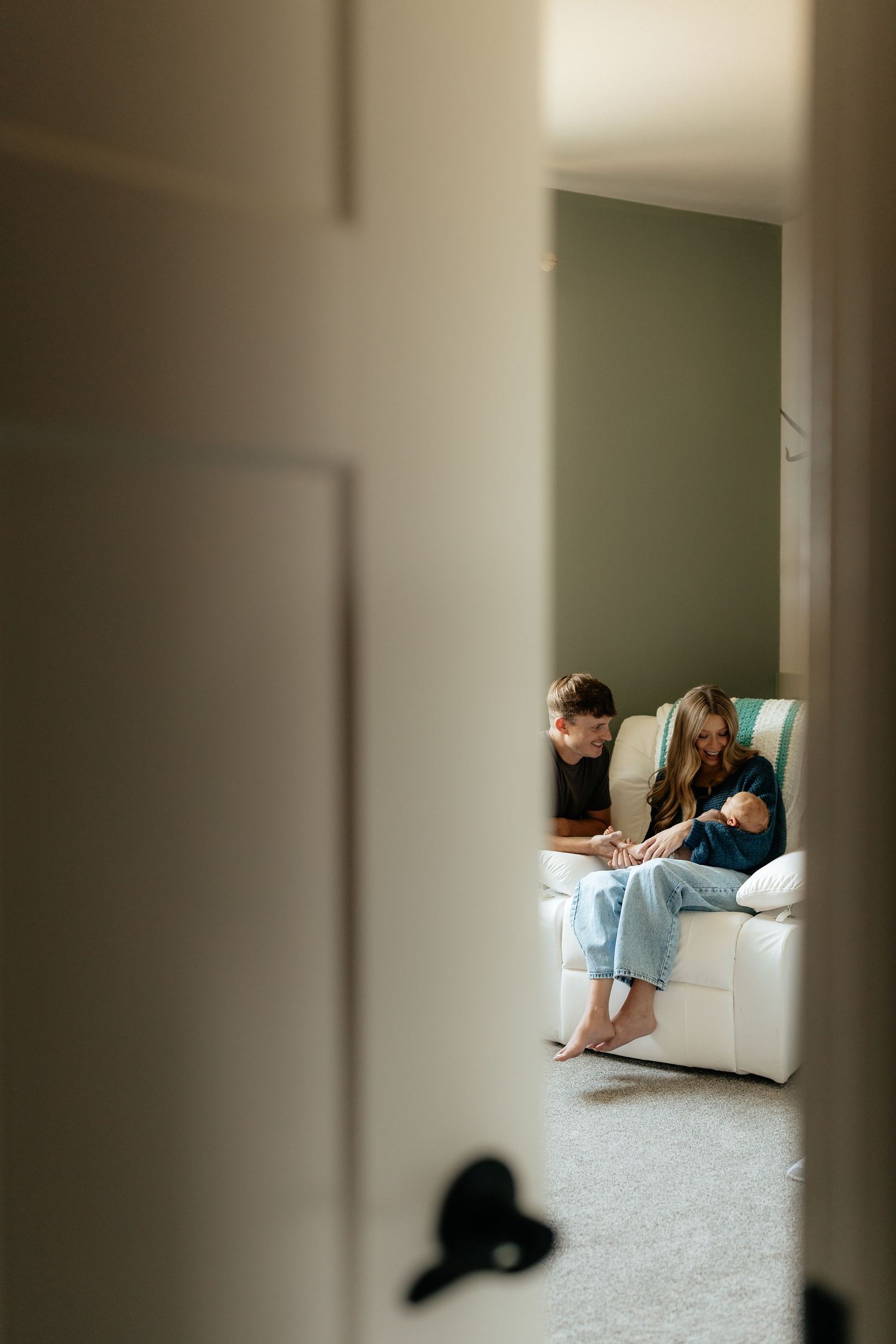 New parents sit on nursery floor admiring their newborn baby in front of a white crib.