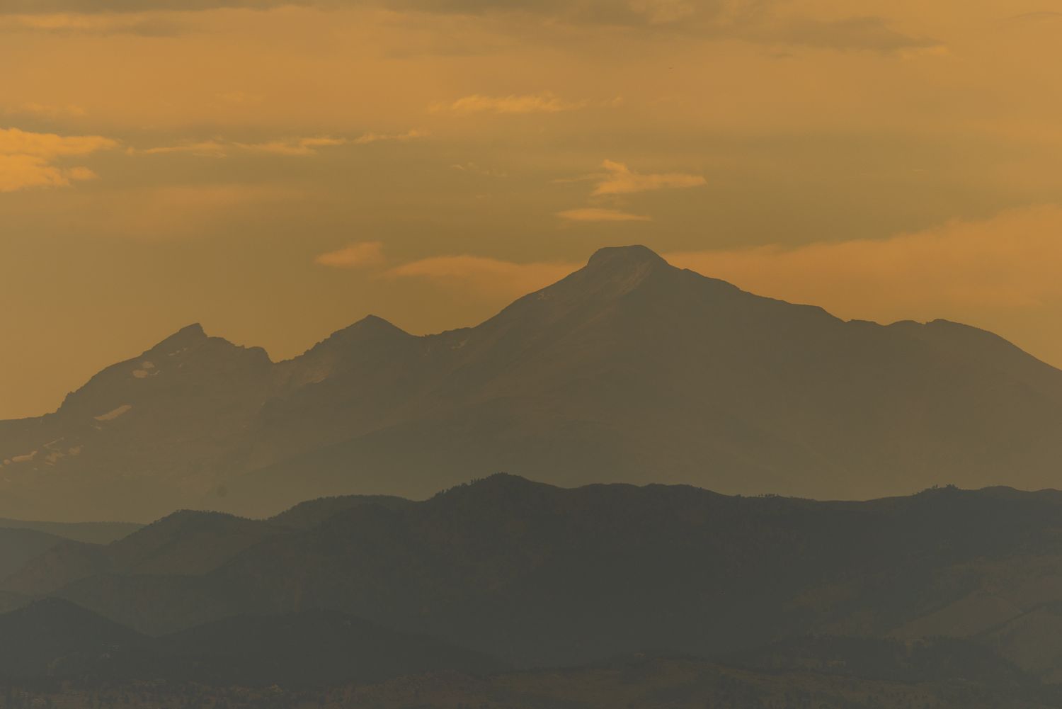 Layered mountain silhouettes at golden sunset with dramatic orange sky.