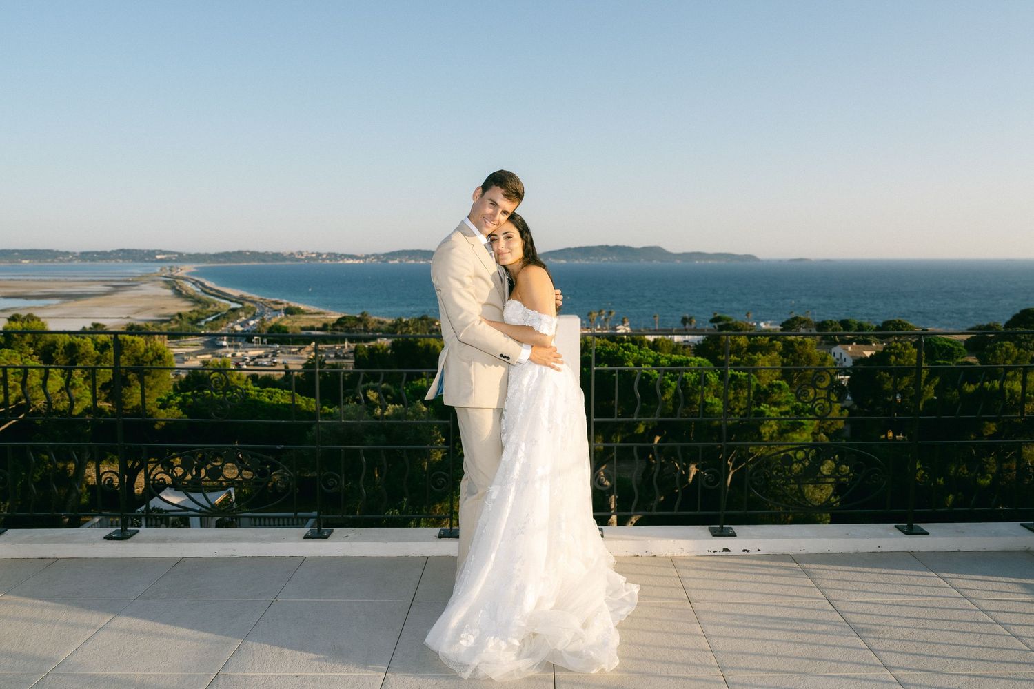 Bride and groom embrace on rooftop terrace with stunning coastal ocean views on their wedding day.