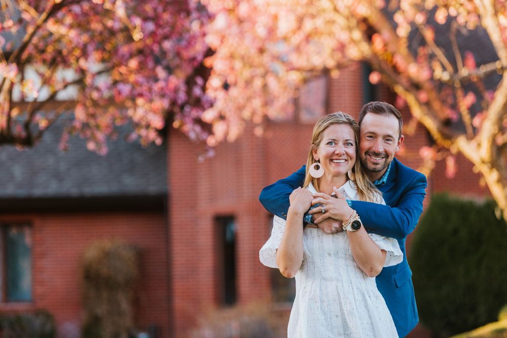 Happy couple embracing outdoors near pink cherry blossom trees and red brick building in spring.