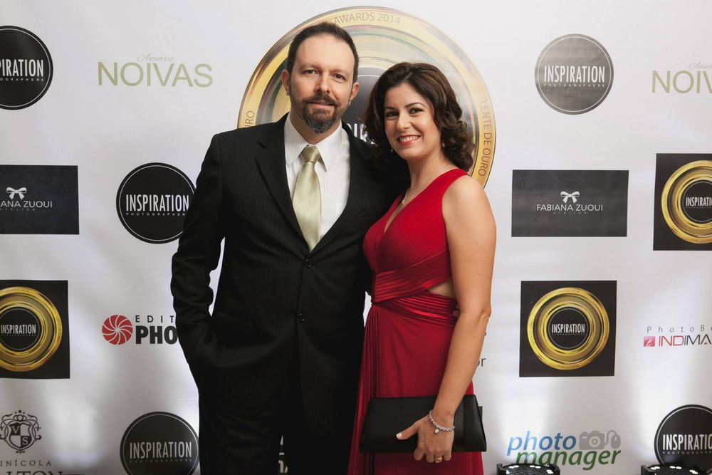 Elegant couple posing on red carpet at Inspiration awards event, man in black suit, woman in red dress.