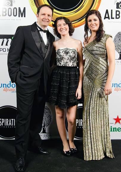 Three elegantly dressed people posing on a red carpet event backdrop with Alboom and Heineken logos.
