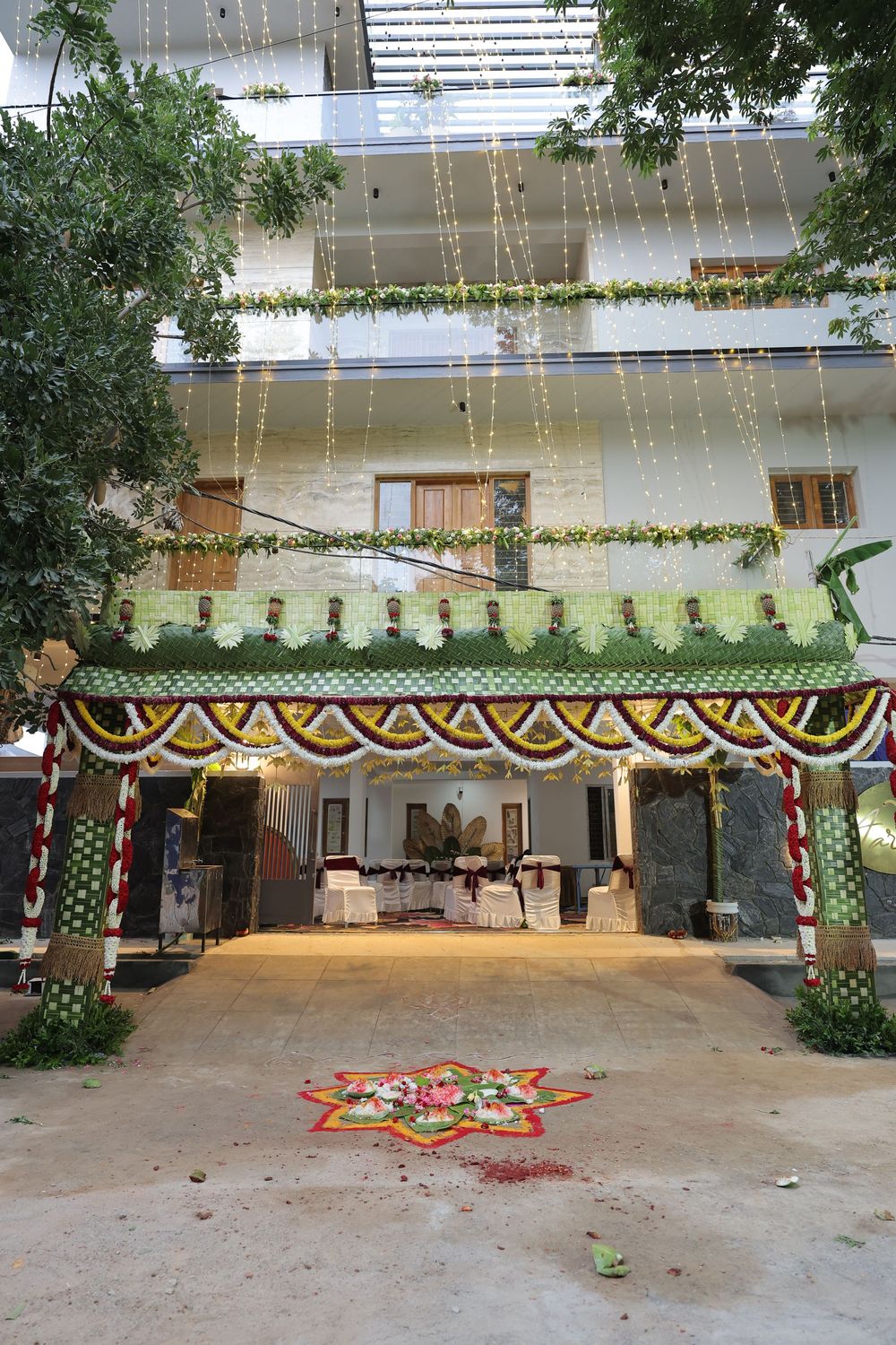 Traditional Indian wedding venue entrance decorated with floral garlands, rangoli, and hanging lights on a multi-story building.