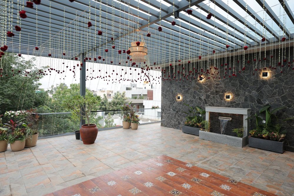 Elegant open-air terrace with stone walls, terracotta tiles, hanging decorations, potted plants, and a modern water feature.