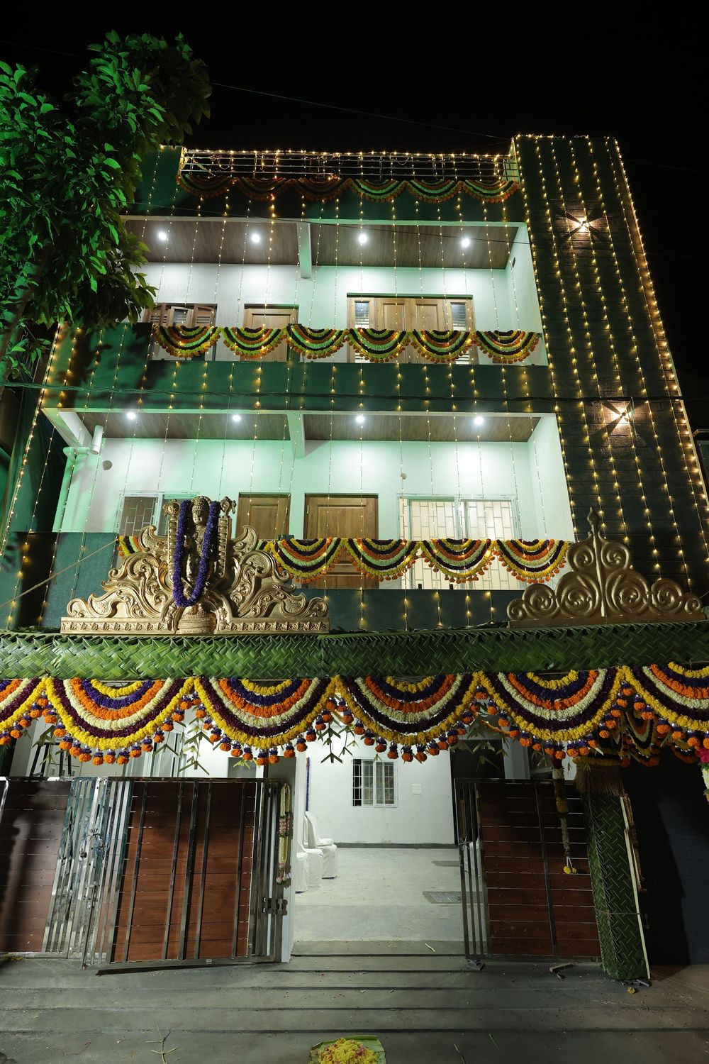 Colorfully decorated Indian building at night with floral garlands, string lights, and festive ornaments for a celebration.