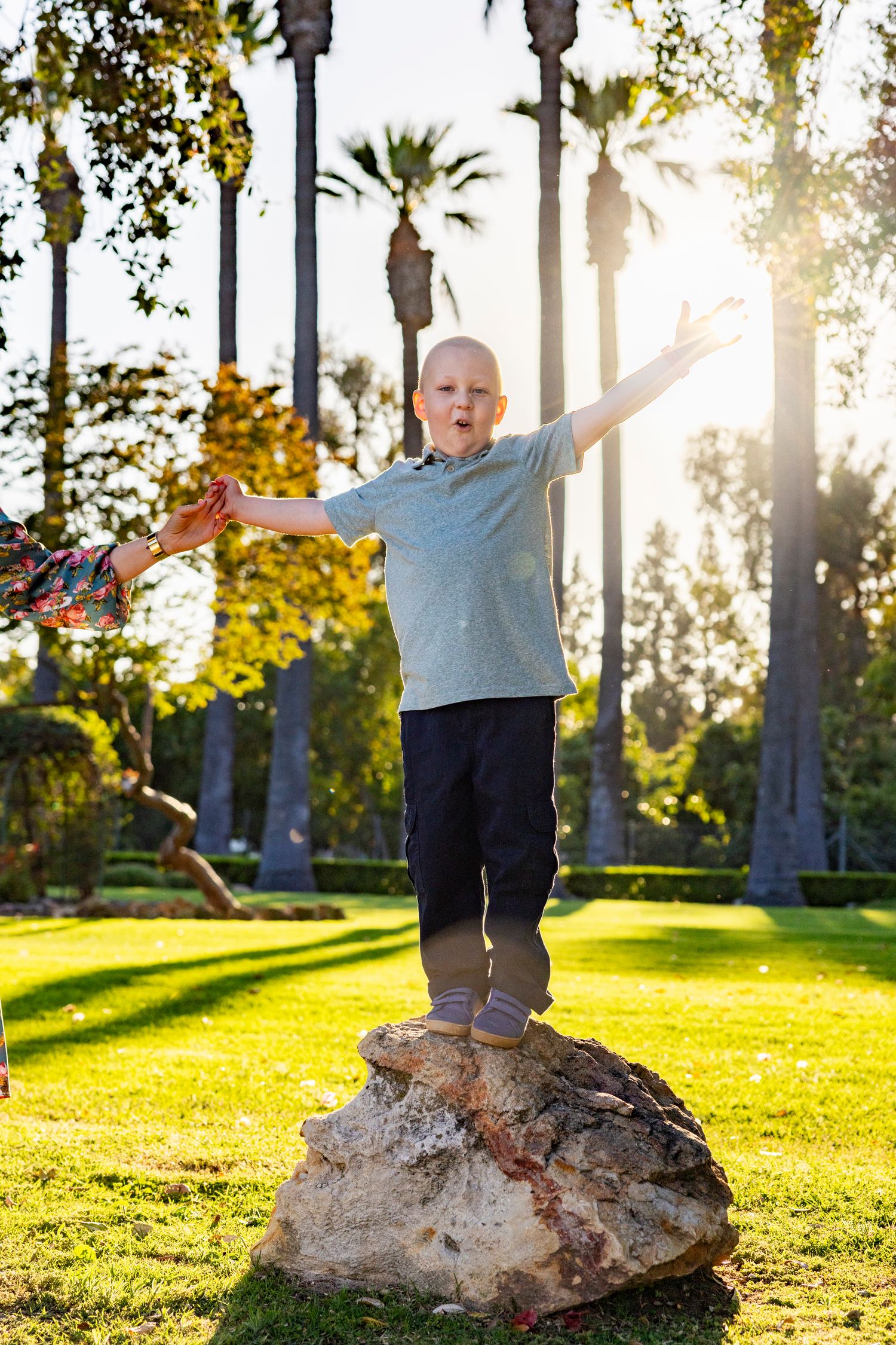 Young boy holding a shiny gold ball above his head on green lawn in front of a white house.