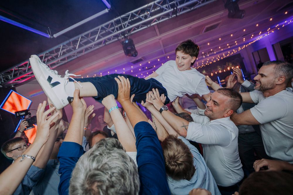 Boy crowd surfing at a lively party event with guests lifting him overhead on a dance floor.