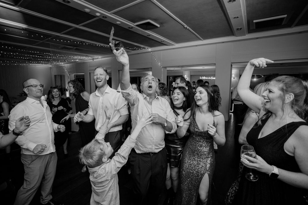 Black and white photo of guests dancing and celebrating joyfully at a lively wedding reception party.