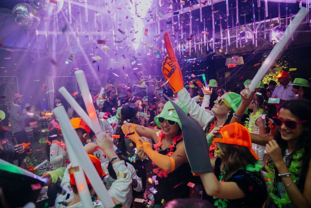 Colorful nightclub scene with crowd dancing under purple lights and confetti.
