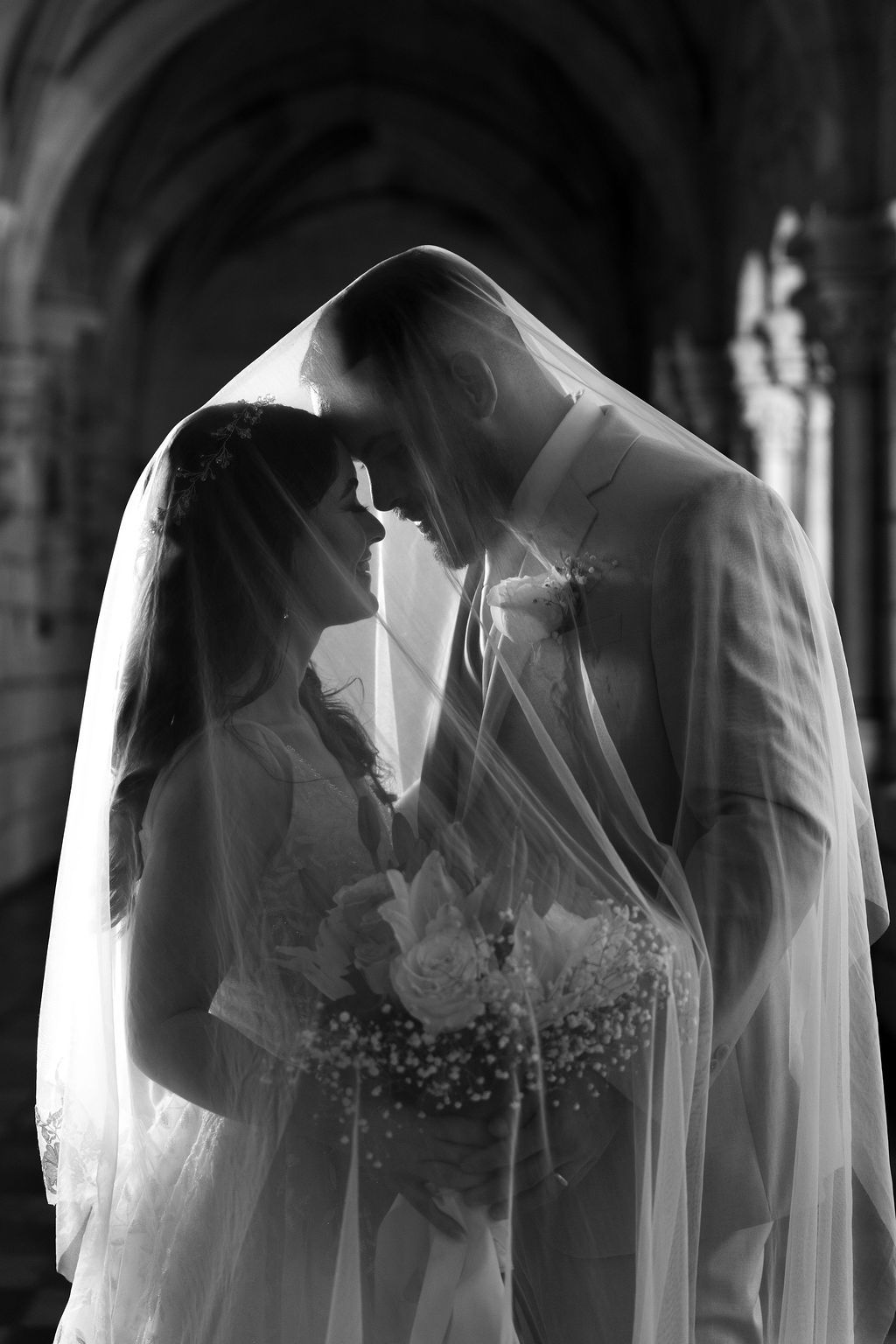 Bride and groom sharing an intimate moment beneath the wedding veil in a timeless black and white portrait by OkataStudio.