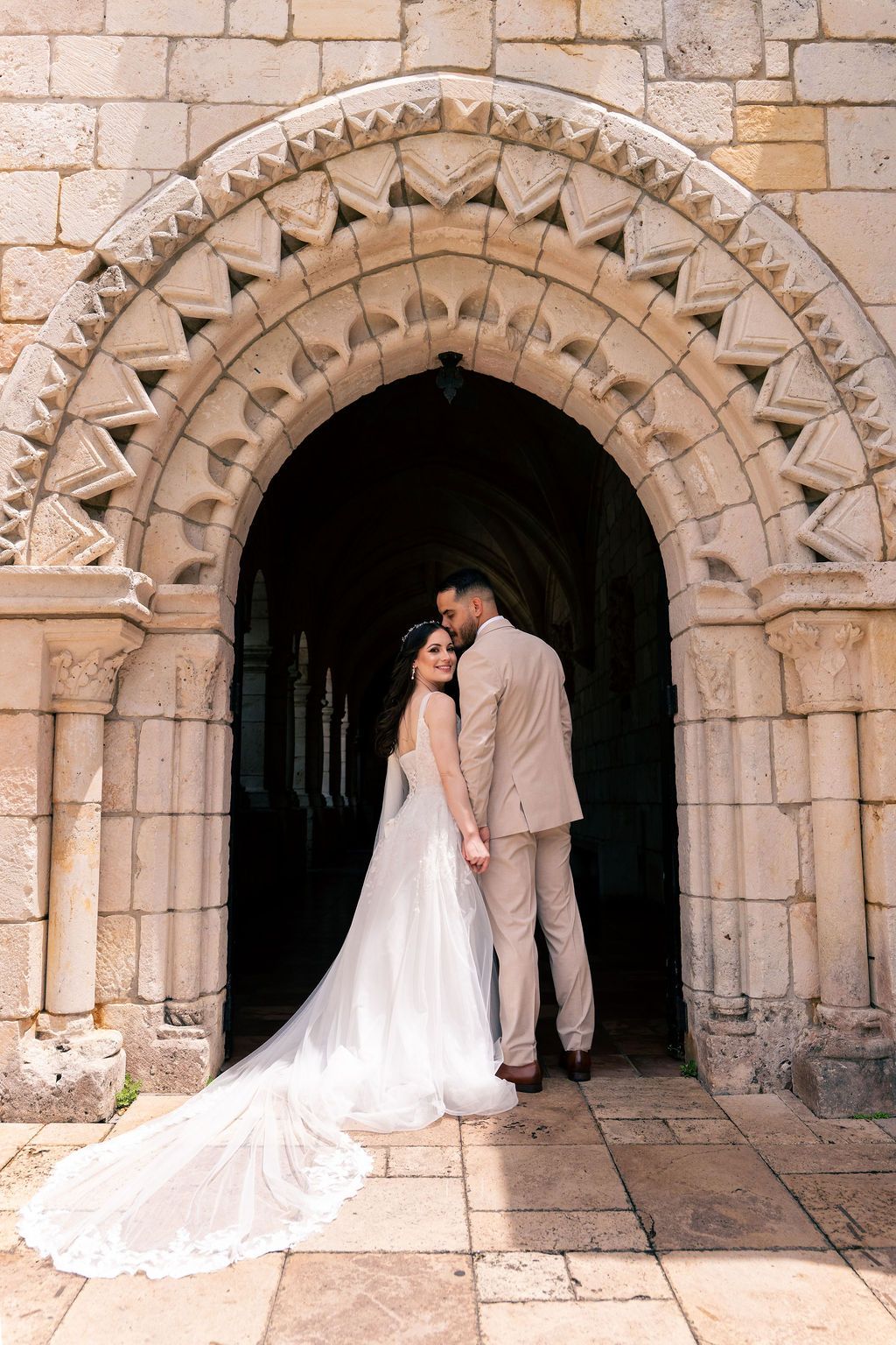 Bride and groom beneath historic stone archway,  Ancient Spanish Monastery during wedding by Miami wedding photographer OkataStudio.