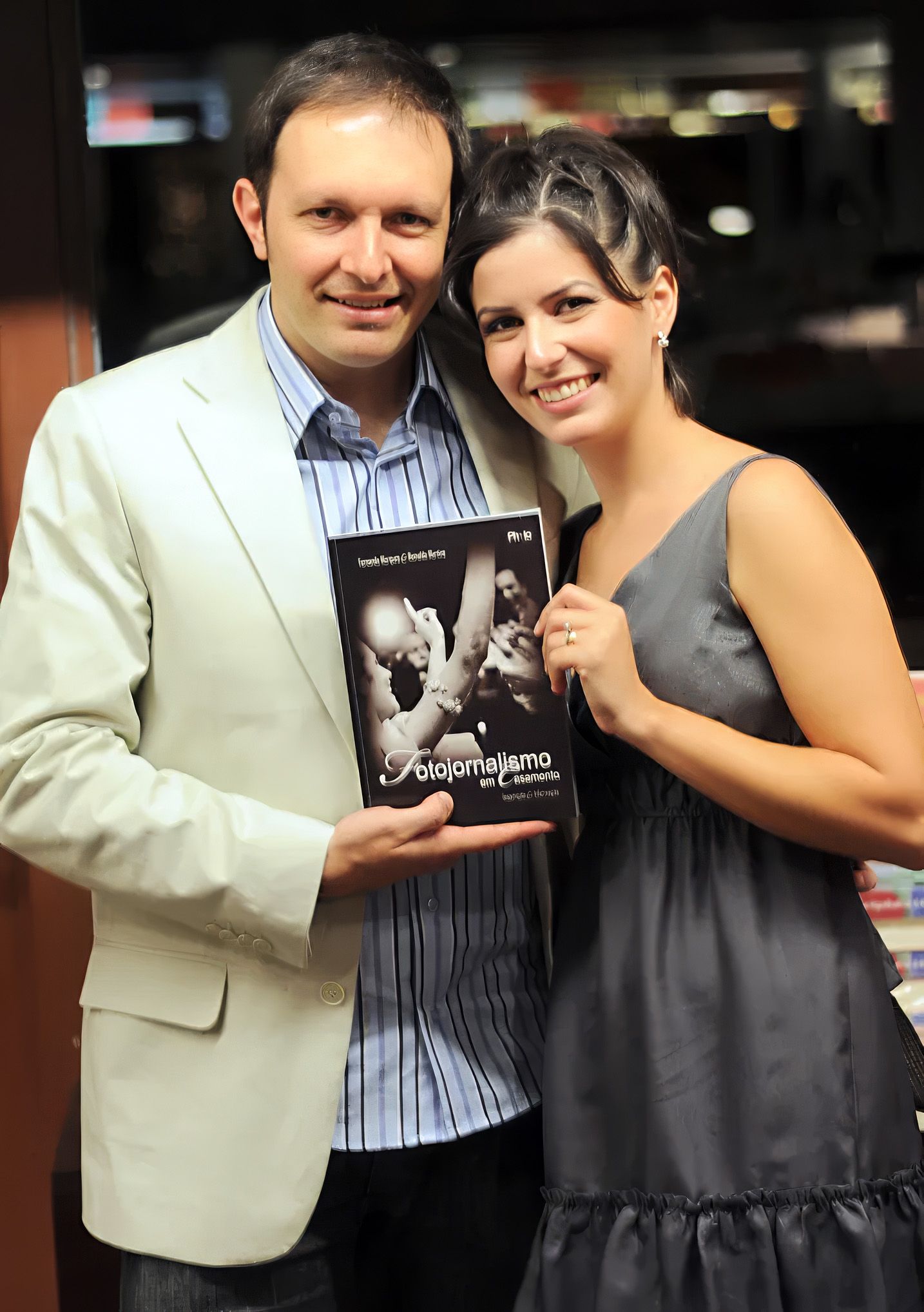 A smiling couple poses together holding a book titled Solojornalismo em Casamento at what appears to be a book launch.