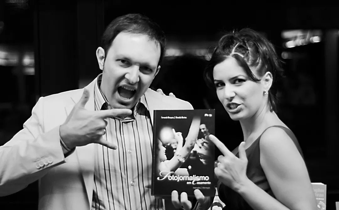 Two people posing with a book, making hand gestures, in a black and white photo at an event.