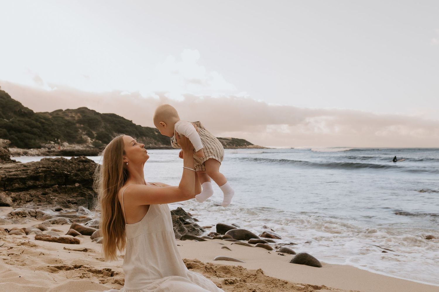 Family of four smiling together on rocky beach at golden sunset with ocean backdrop.