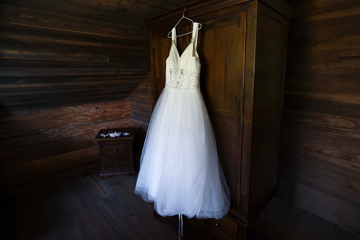 White lace ballgown wedding dress hanging on wooden armoire in rustic cabin bridal suite.