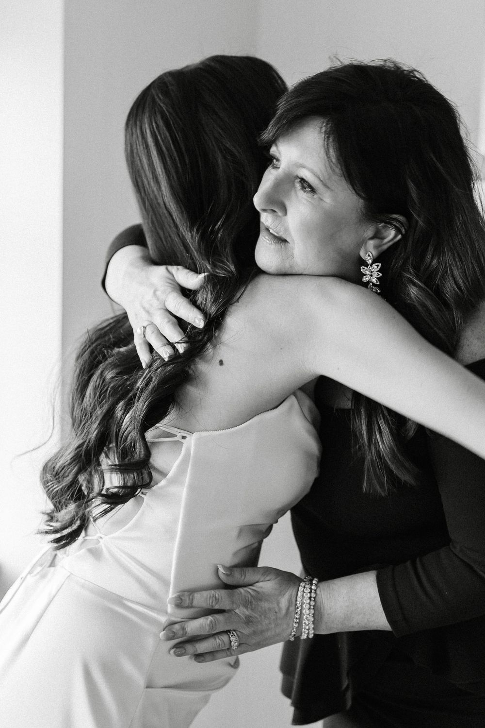 Black and white photo of a bride in a white gown sharing an emotional hug with her mother on her wedding day.