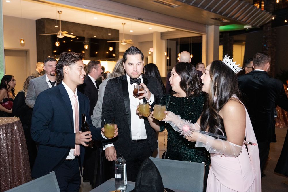 Elegantly dressed guests socializing at a formal evening gala event, holding drinks and wearing formal attire.