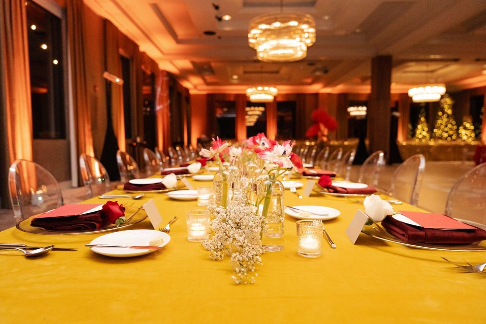 Elegant banquet hall with gold tablecloth, red napkins, floral centerpieces, and crystal chandeliers for a formal event.