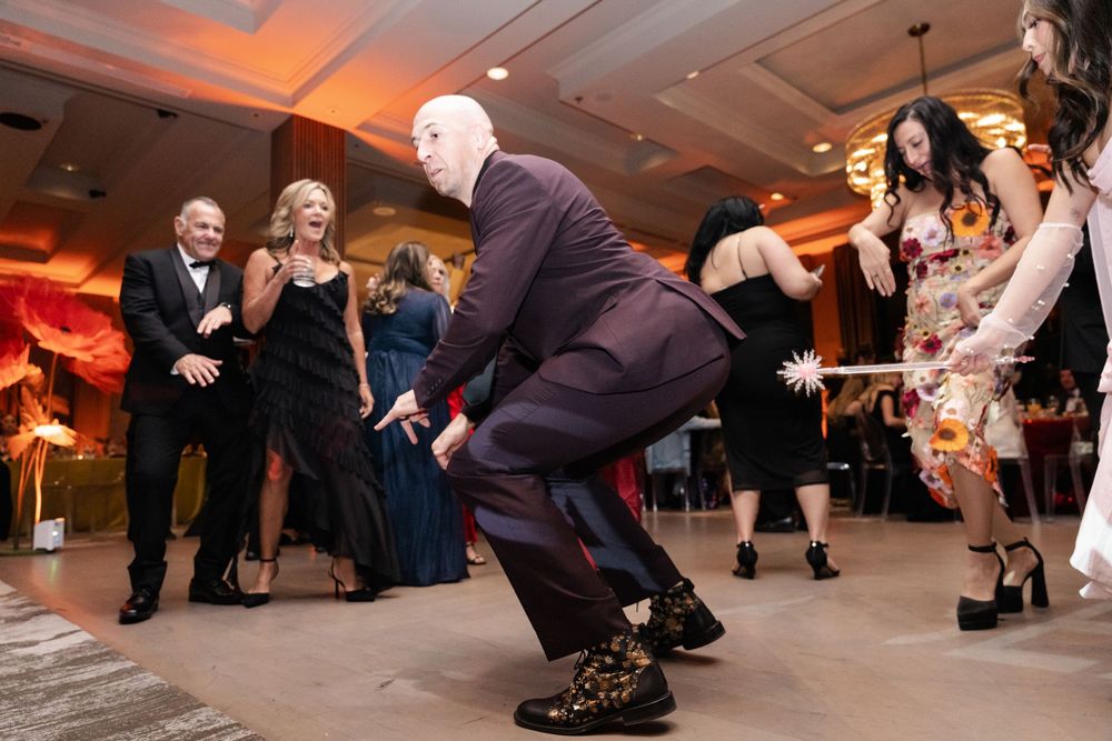 Guests dancing energetically at a formal wedding reception on a white dance floor with warm ambient lighting.