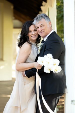 Elegant bride and groom posing together holding white orchid bouquet with ribbon on their wedding day.