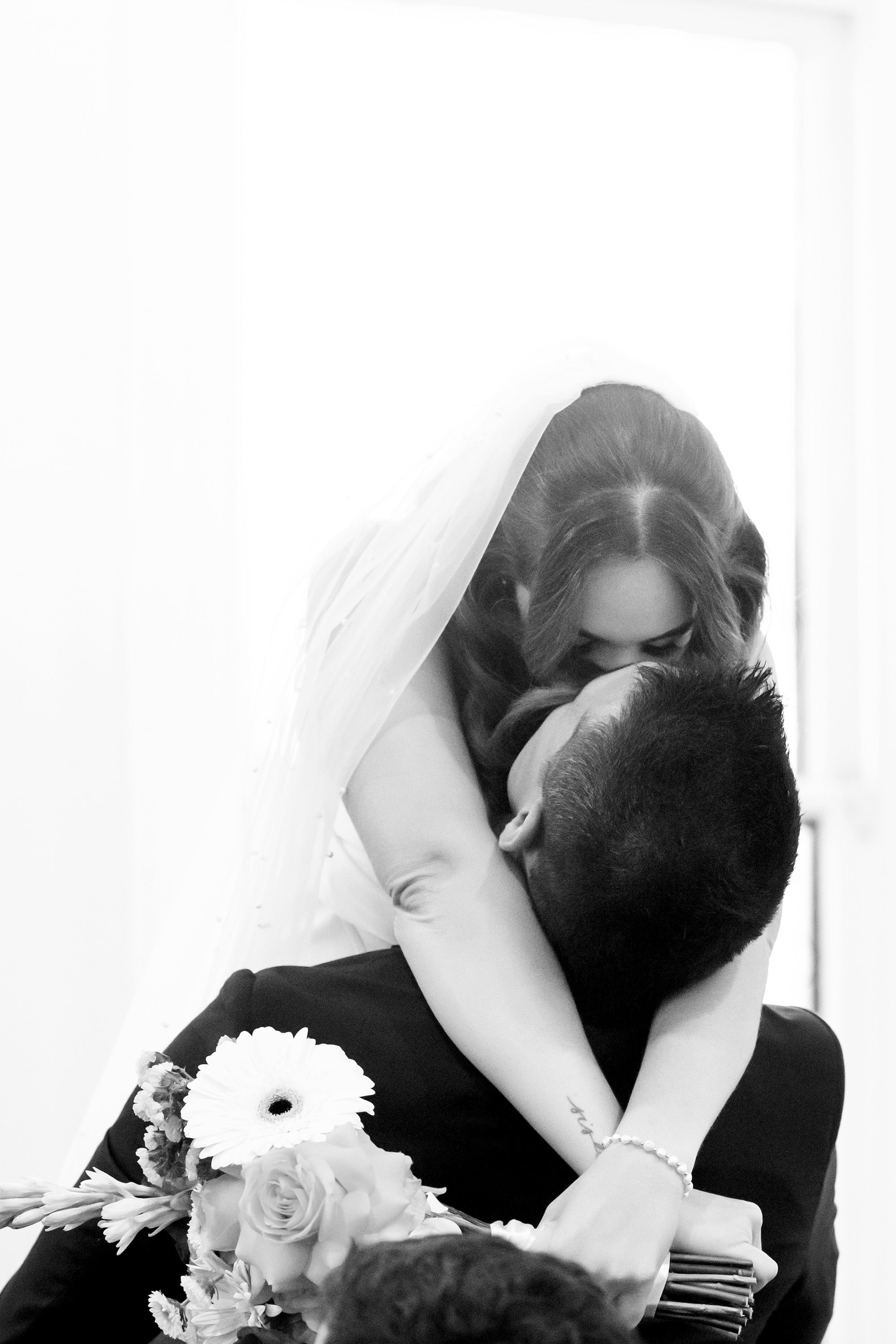 Black and white photo of a bride and groom sharing a tender embrace, with the bride holding a bouquet of white flowers.