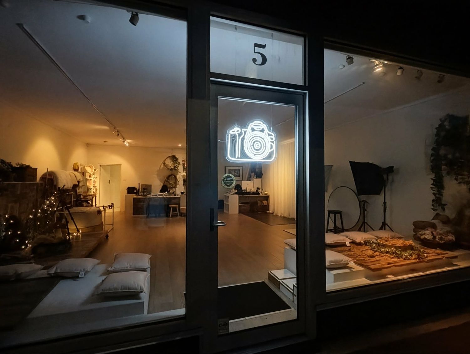 Photography studio storefront at night with neon camera sign, number 5 above door, warm interior lighting visible.