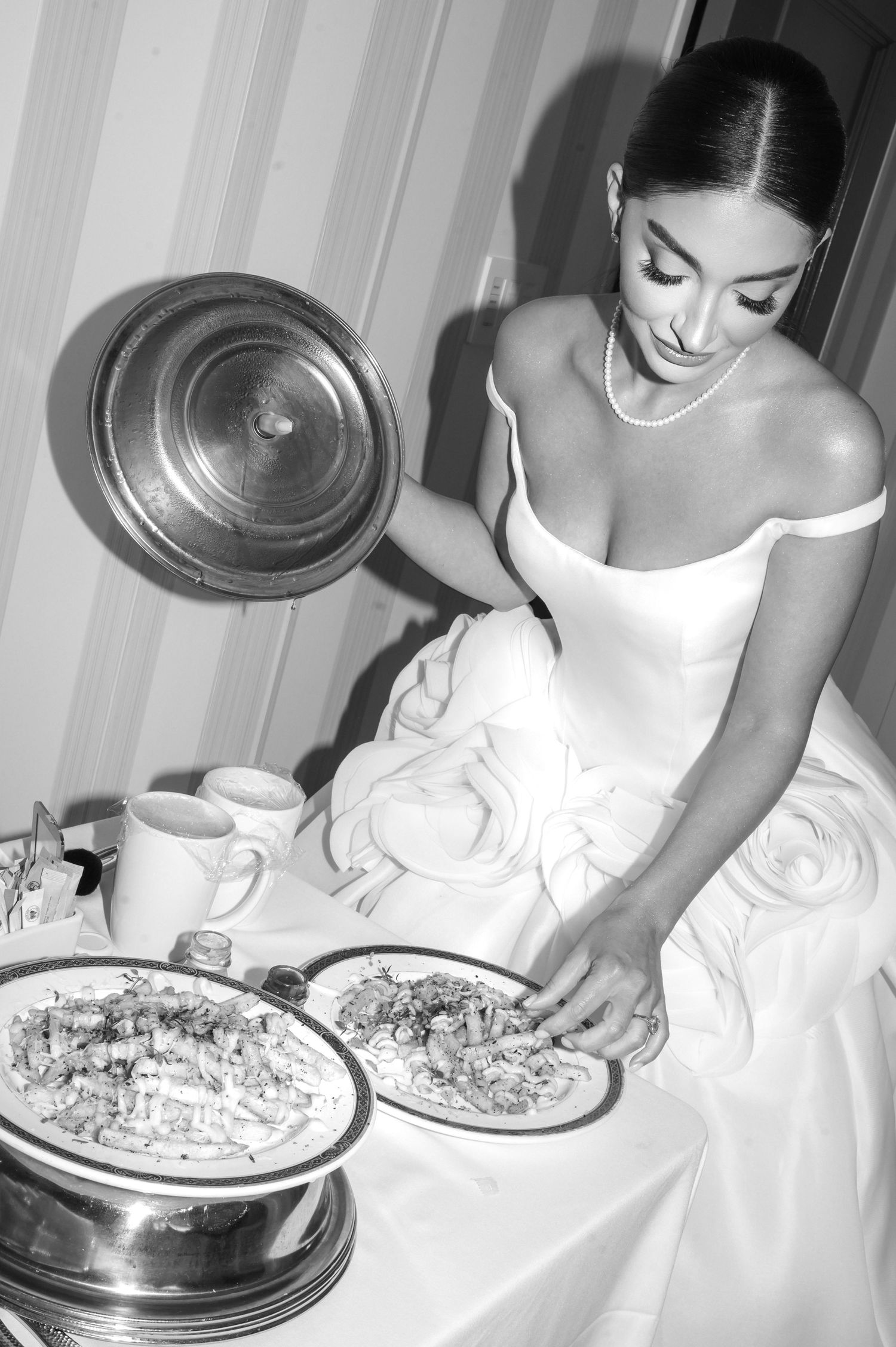 Elegant bride in white dress holding martini glass with olive skewer, wearing pearl necklace and diamond ring.