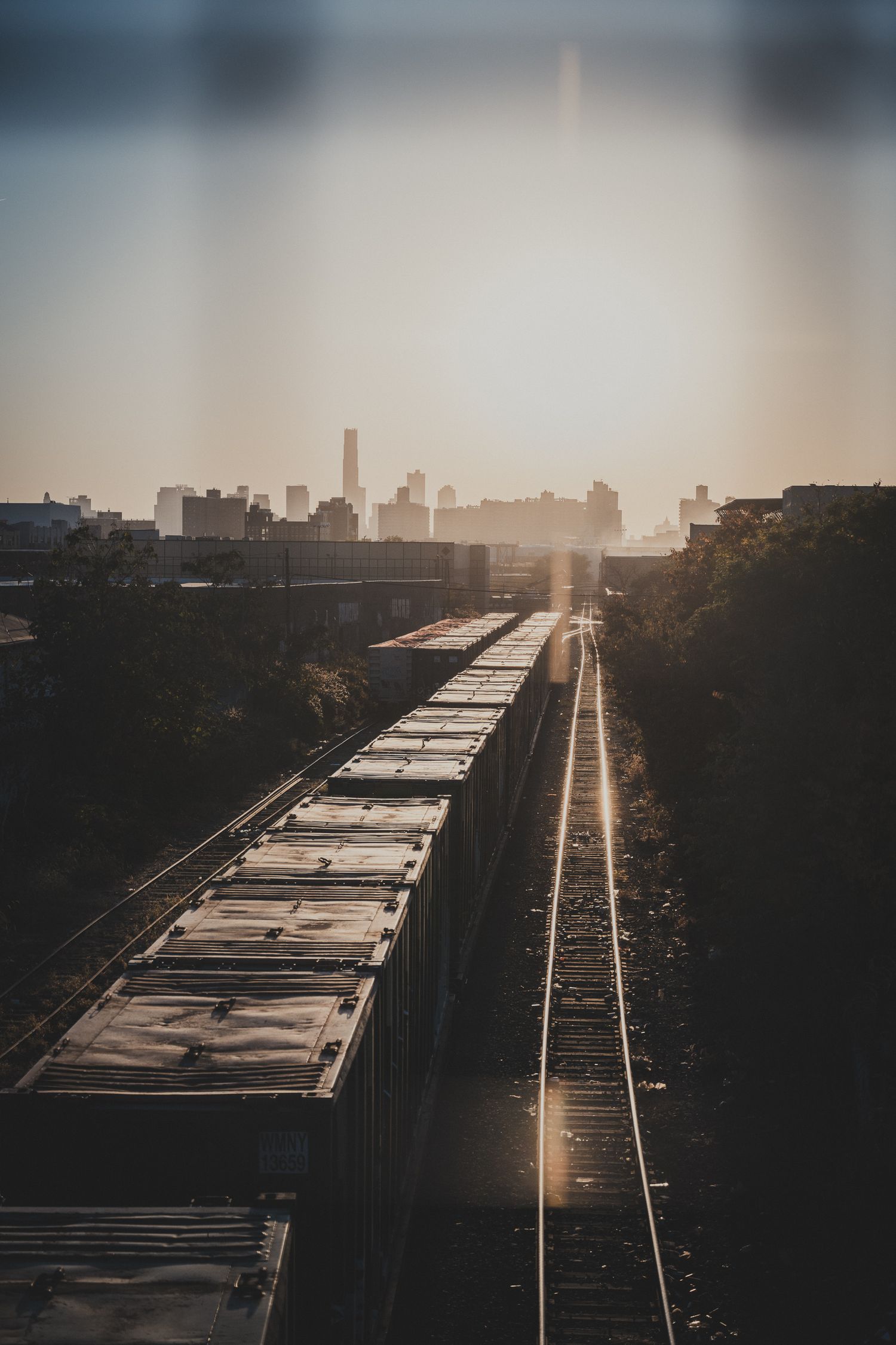 Binari ferroviari con vagoni merci e skyline di New York sullo sfondo al tramonto