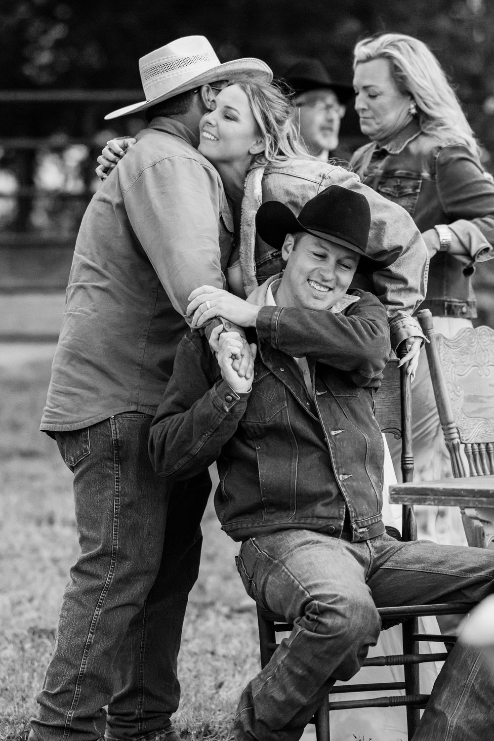 Black and white photo of cowboys and cowgirls in western wear sharing a joyful moment at an outdoor ranch event.