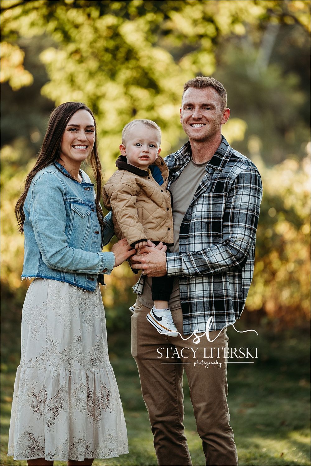 Family portrait of smiling parents holding toddler outdoors, photographed by Stacy Literski Photography.