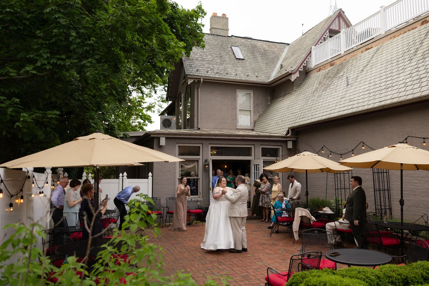 Outdoor wedding reception at elegant historic venue with guests mingling on patio under yellow umbrellas.